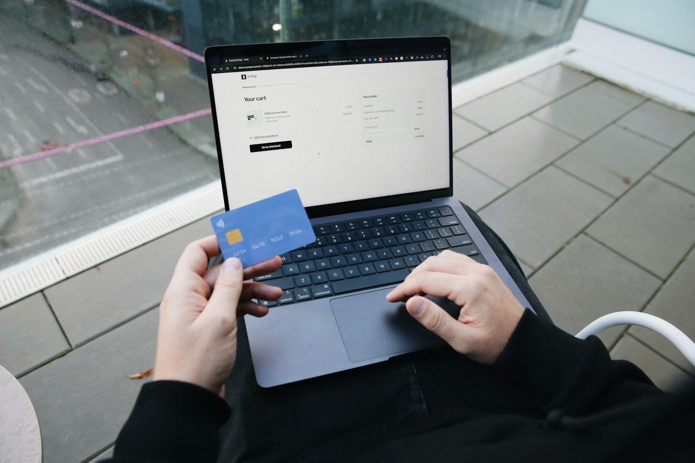 Hands holding a phone and payment card beside a laptop